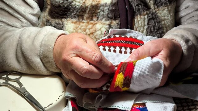 A woman works a needle on a piece of fabric with different colored threads in a piece of fabric with a needle