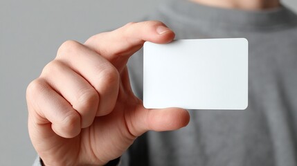 Person holding a blank white card with rounded corners, presenting a clean slate in front of a gray background. Space for custom content.