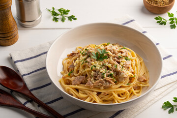 Spaghetti carbonara with Canned tuna topped with parmesan cheese and parsley in white plate.