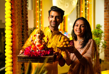 Indian Couple Holding Ganesh Idol and laddu Thali with Joyful Expressions During Ganesh Festival
