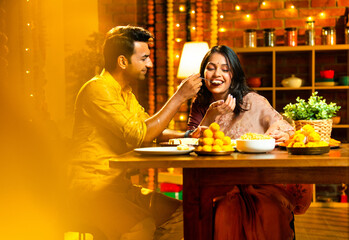 Couple serving food and sweets on Diwali night, sitting together in ethnic dress at dining table