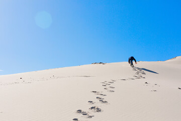 A child scrambles up a sandy mountain, leaving a trail behind him against a blue sky with a glare. Concept of hard work. Explorer, hiking