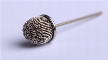 Delicate wire mesh sphere attached to a metal pin resting on a smooth surface