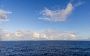 Serene Ocean View with Blue Sky Clouds and a Distant Rainbow