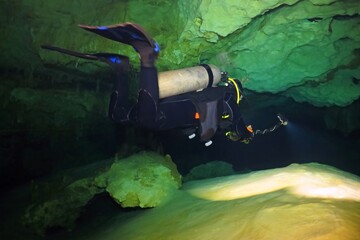 Scuba diver exploring underwater cave with camera and lights. Diver swimming with lights in the flooded tunnel. Underwater speleology in the cenote. Tourist with equipment in the cave.