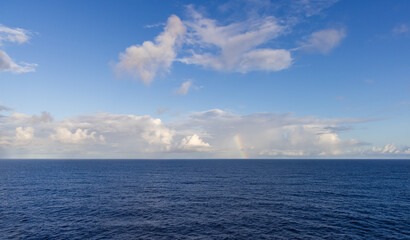 Serene Ocean View with Cloudscape and Rainbow in a Clear Blue Sky