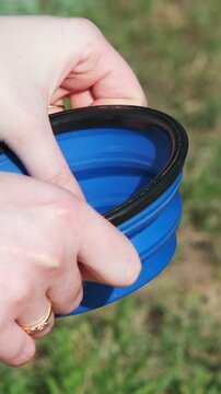 Girl unfolds a collapsible silicone bowl for animals and puts it down. Close-up. Traveling with animals. Walking on a sunny day in a city park. Care concept, animal life
