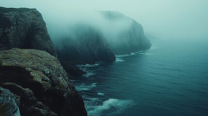 Misty coastal cliffs meet a dark ocean expanse.