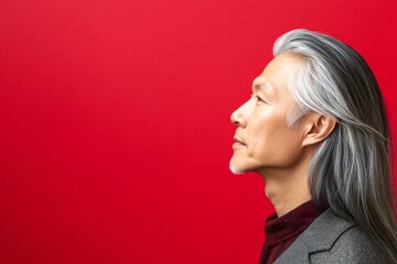 Fototapeta premium Trendy men's undercut haircut - midlife asian man with long hair. Red solid background. Pattern of style for aging men. A professional studio photography session of a stunning man.
