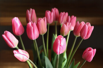 Fototapeta premium Pink tulips bouquet close up on warm dark wooden background, fresh spring flowers arrangement, mothers day and international womens day greeting card background with copy space.