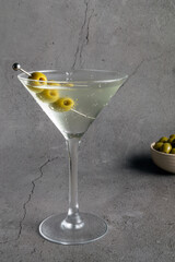 a clear vodka martini in a stemmed glass, garnished with three green olives on a pick. A small bowl of olives is partially visible in the background