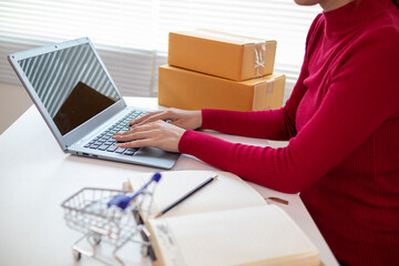 Asian businesswoman in red shirt is checking product orders and calculating sufficient stock to deliver to customers according to orders entered into online shopping application.Copy Space for text