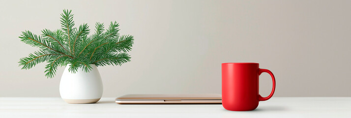 Red mug, pine branches in vase and closed laptop on white desk with neutral background