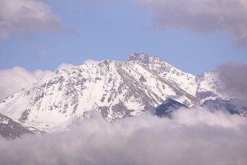 Obraz premium a cloud over a forest and a snowy mountain peak during sunset