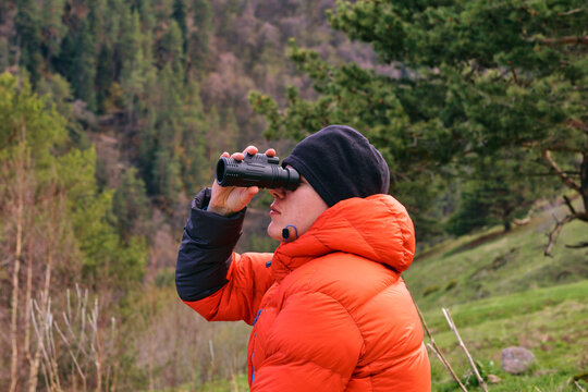 A man looks intently at the mountains through a monocular