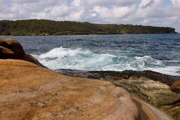 Rocky coastal shoreline with ocean waves and a forested background. Ideal for travel, nature, or...