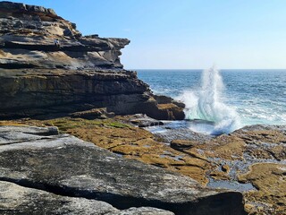 A wave splashes dramatically against rugged  coastal rocks, dividing the horizon line.