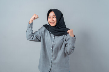 Portrait of a young Muslim woman in a black hijab and grey shirt confidently smiling while showing...