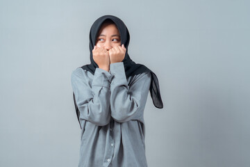 Young Asian Muslim woman wearing a black hijab and gray shirt poses with clenched fists near her...