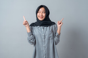 Portrait of a cheerful young Asian Muslim woman wearing a black hijab and grey shirt, smiling while...