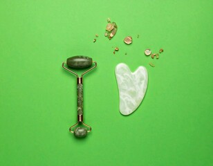 Green roller and gua sha, skincare tools on matching background