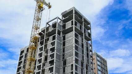 Fototapeta premium Building crane and building under construction against blue sky