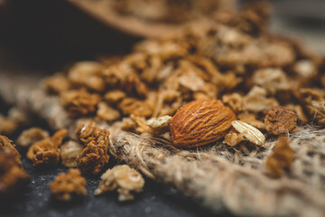 Close-up of granola and almond on a rustic textile surface. Macro view highlighting texture and detail of healthy breakfast ingredients with natural warm tones