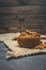 Wooden bowl filled with granola and nuts placed on a rustic burlap mat. Natural healthy breakfast concept with organic textures and warm earthy tones