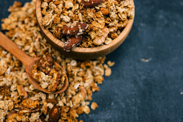 Granola and nuts in a small wooden spoon with a blurred bowl in the background. Rustic style breakfast concept with healthy ingredients on dark surface