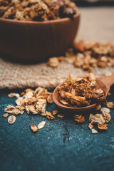 Granola and nuts in a small wooden spoon with a blurred bowl in the background. Rustic style breakfast concept with healthy ingredients on dark surface