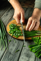 Hands skillfully slice green onions on a wooden cutting board. Nearby, freshly chopped herbs and whole green onions are neatly arranged, showcasing vibrant colors in a cozy kitchen setting