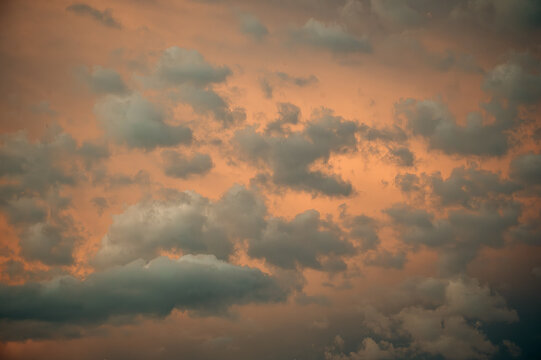 Fluffy white and grey clouds float over a moody orange sky - Powered by Adobe