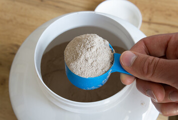 Male hand holding scoop of whey protein. Preparing protein shake