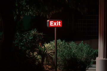 An illuminated exit sign guides the way out in the dark of night. The red glowing sign stands out against the surrounding darkness.