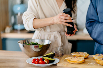 Close up of unrecognizable woman seasoning salad while preparing healthy breakfast in kitchen
