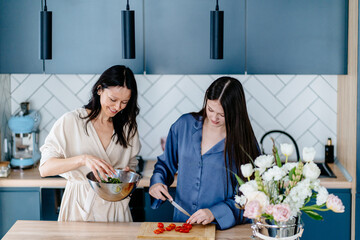 Mother and teenage daughter preparing salad and cutting tomatoes together