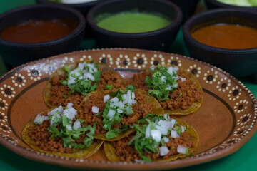 A mouthwatering plate of tacos filled with spiced longaniza and garnished with lush cilantro and onions, accompanied by vibrant salsas and fresh lime wedges for a tasty experience.