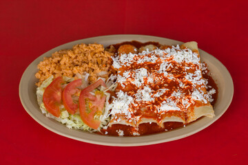 An enticing plate of flavorful entomatadas topped with cheese and sauce, served alongside rice and a refreshing salad, celebrating the richness of Mexican culinary traditions.