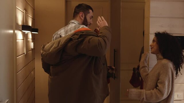 A man stands and takes off his jacket while talking to a woman standing across from him, they give each other a high five while two friends stand next to them, in the hallway
