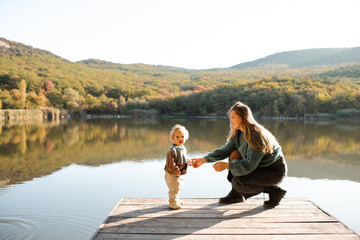 Young woman holding baby girl 1 year old wearing knitted sweaters over nature landscape view....