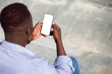 African American guy holding smartphone with blank screen on stone staits outside, mockup for mobile app design