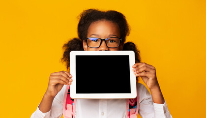 African American Schoolgirl Hiding Behind Tablet Blank Screen Over Yellow Studio Background. Mockup