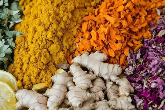A vibrant display of turmeric powder, ginger root, dried petals, and lemon slices arranged together