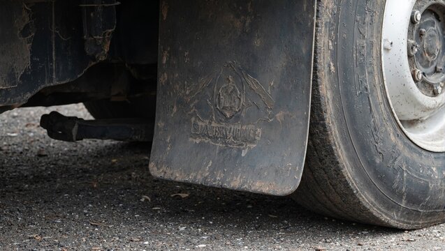 Close up shot of a weathered tractor trailer mud flap featuring a curled edge embossed logo and traces of road grime