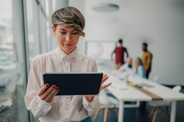 Businesswoman using digital tablet in modern office with colleagues working in background
