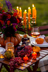 Beautiful elegant autumn table setting for thanksgiving family dinner or wedding. Orange pumpkin with flowers as centrepiece. Cozy fall home atmosphere. Wineglass, romantic marriage proposal, sunset