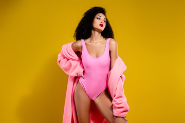 Obraz premium Elegant woman in pink swimwear with matching coat on bright yellow background, exuding glamour, sensuality, and style