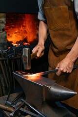 A skilled blacksmith hammers red-hot metal on an anvil sparks flying in a traditional forge. The warm glow of the fire contrasts with the cool evening shadows surrounding the workspace.
