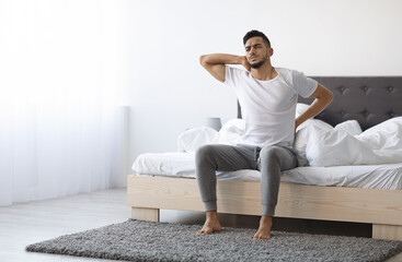 Uncomfortable Bed. Arab Man Waking Up With Neck And Back Pain, Young Middle Eastern Male Suffering...