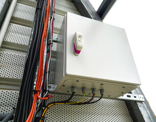 Mounted electrical control box with labeled lock and connected multicolored cables, installed on a perforated metal panel alongside bundled wiring and a ladder-like cable tray